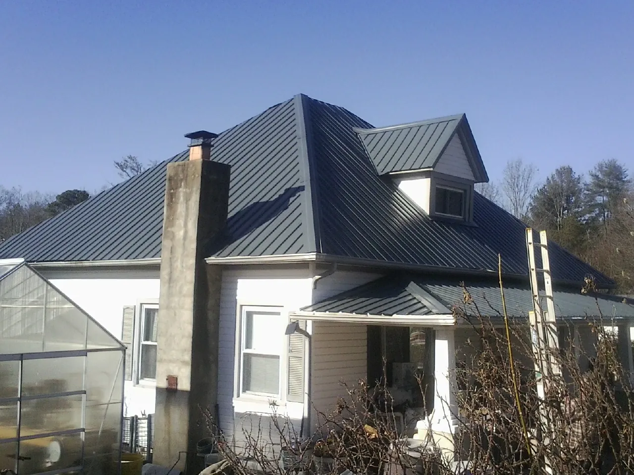 Dark blue standing seam metal roof on a white farmhouse with dormer — Slate & Tile Roof Repair by Roofing Brothers in Rock Port