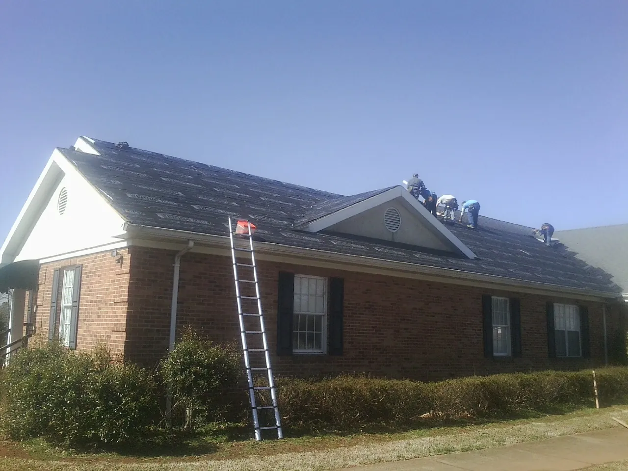 Crew tearing shingles off a brick ranch roof with a ladder set — Emergency Roof Repair work by our crew in Rock Port