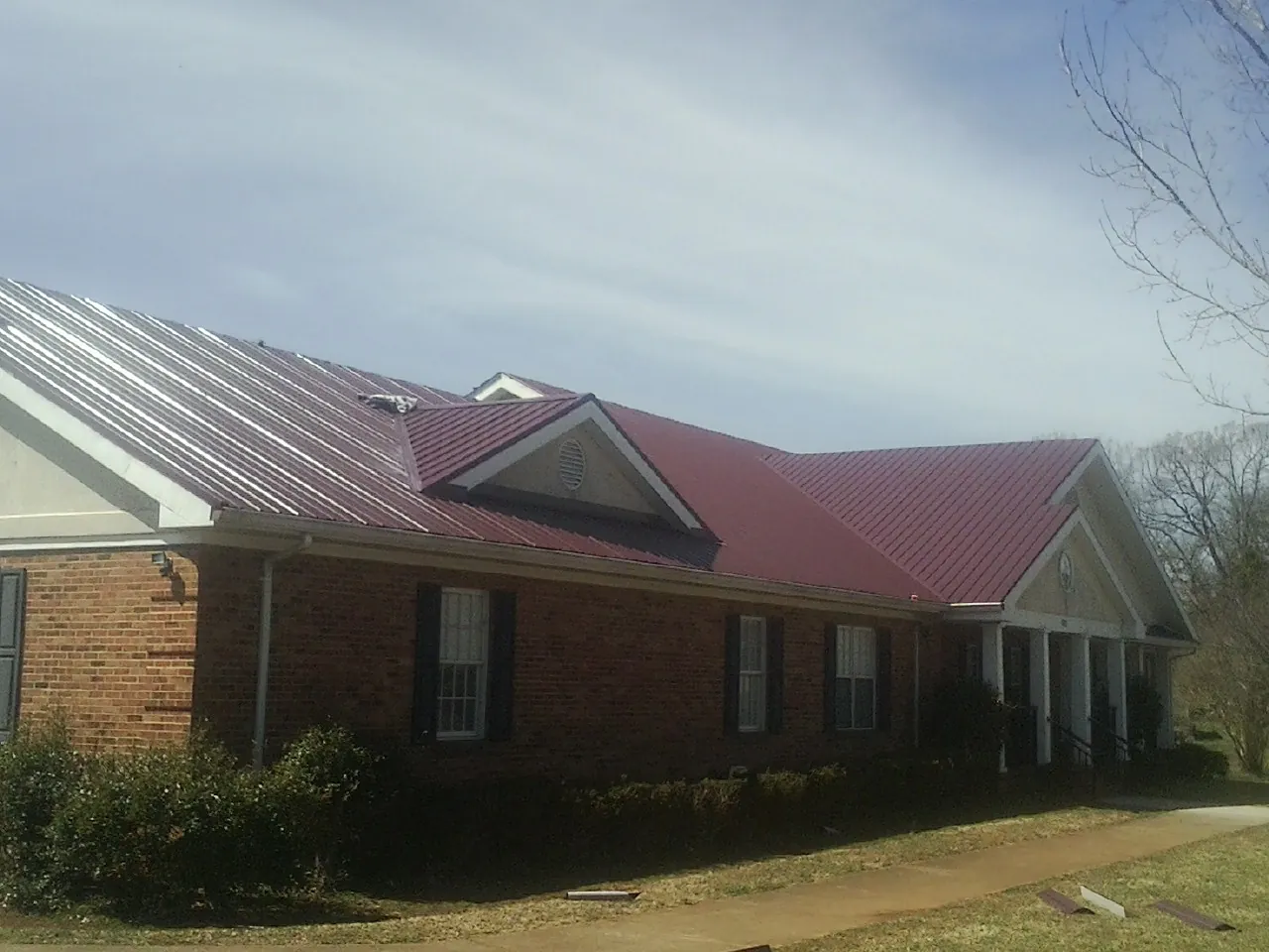 Red metal roof with gabled entries on a long brick building, from a Hail Damage Roof Repair job in Rock Port