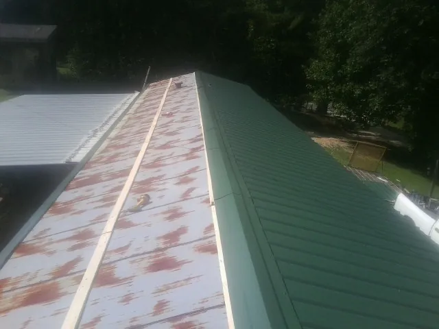 Old rusted panels beside newly installed green metal roofing — Wind Damage Roof Repair by Roofing Brothers in Rock Port