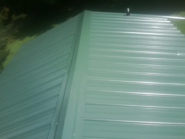 New green metal panels meeting at the ridge of a roof — Flat Roof Repair work by our crew in Rock Port