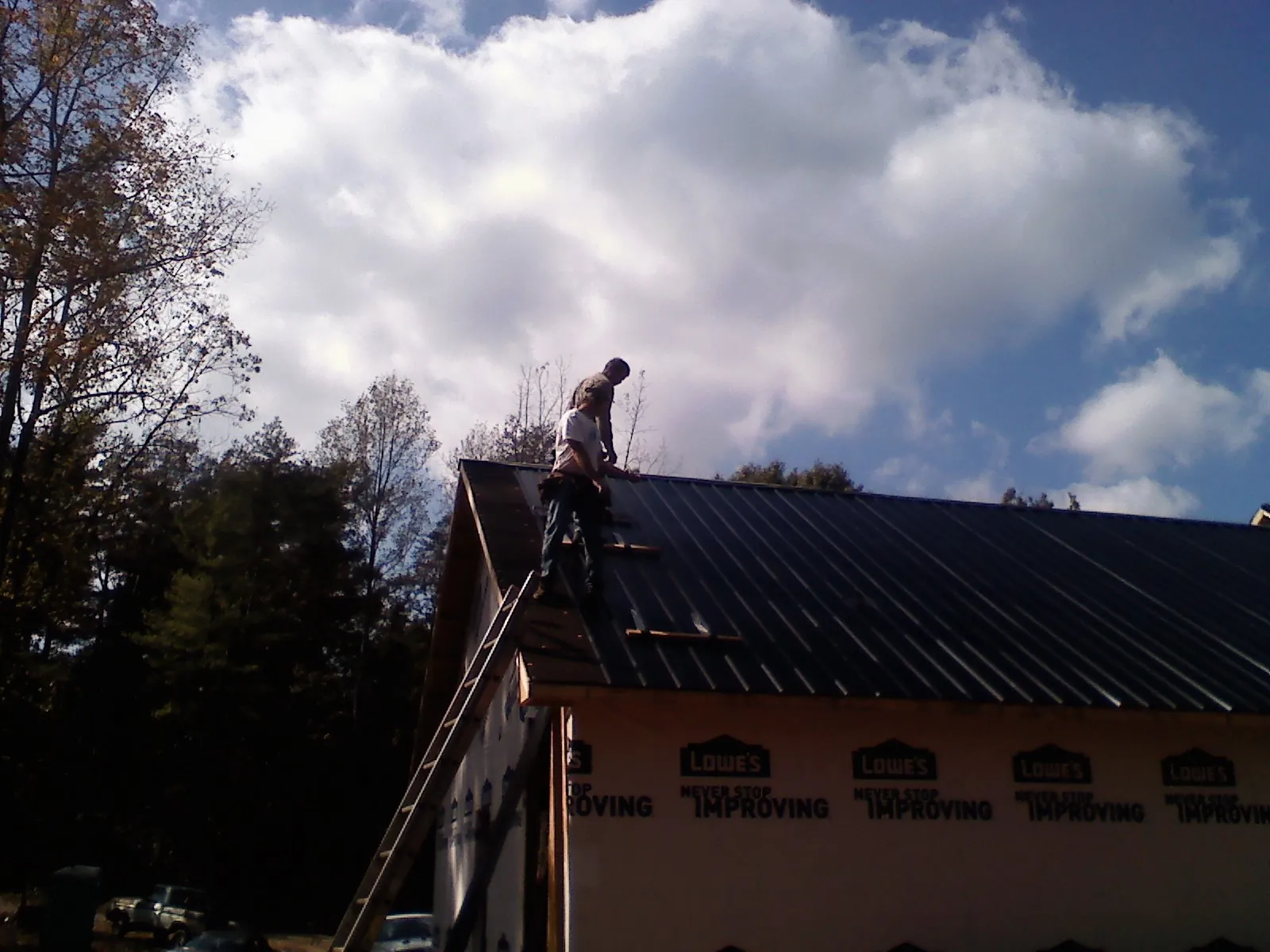Roofer fastening dark metal panels high against a cloudy sky, from a Roof Inspection job in Rock Port