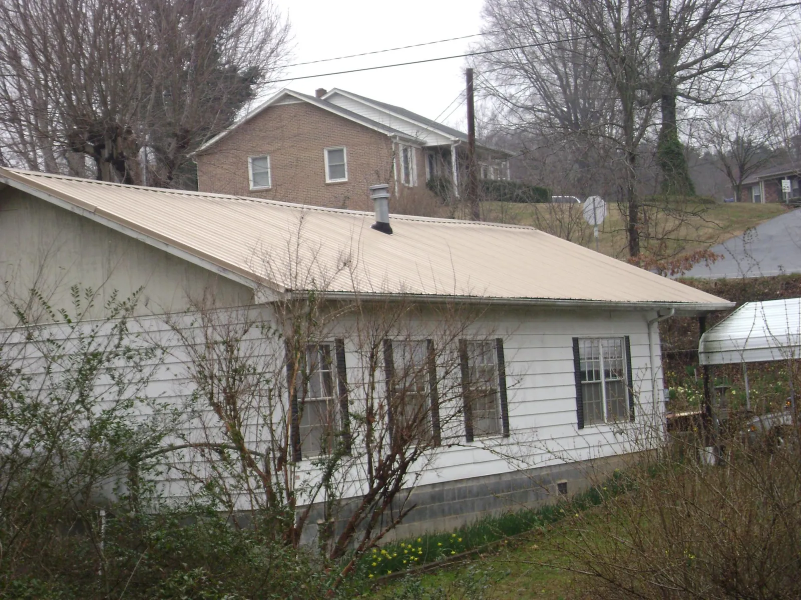 Tan metal roof on a white sided house set into a hillside — Commercial Roofing by Roofing Brothers in Rock Port